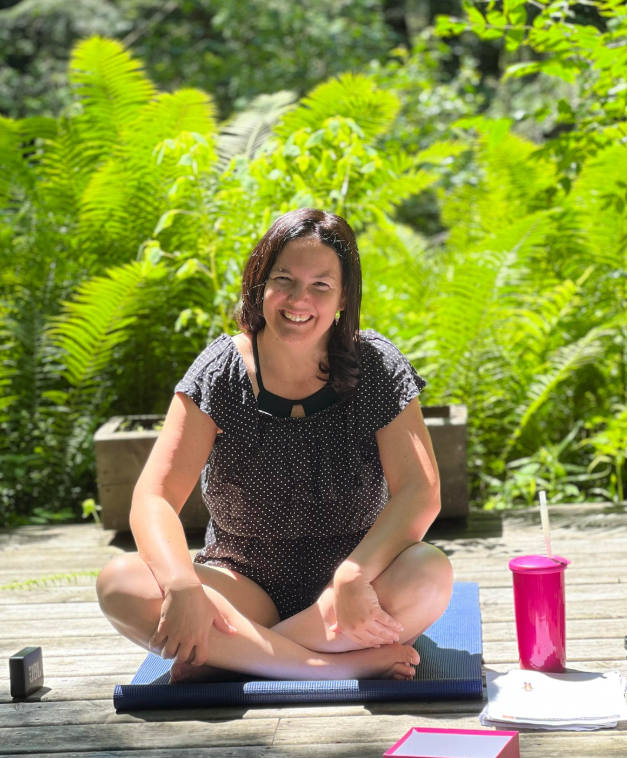 Evelyne Desrochers assise en tailleur sur un tapis de yoga, entourée de fougères.