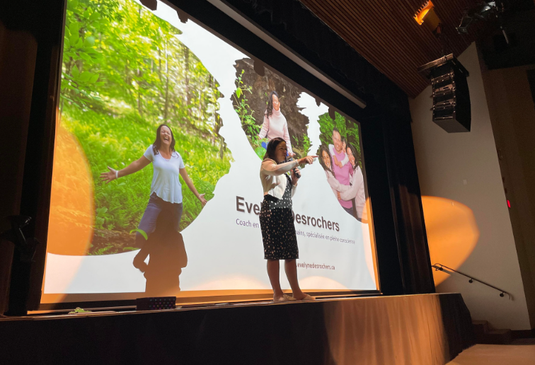 Evelyne Desrochers, coach en pleine conscience, donne une conférence sur scène devant un grand écran illustrant son travail.
