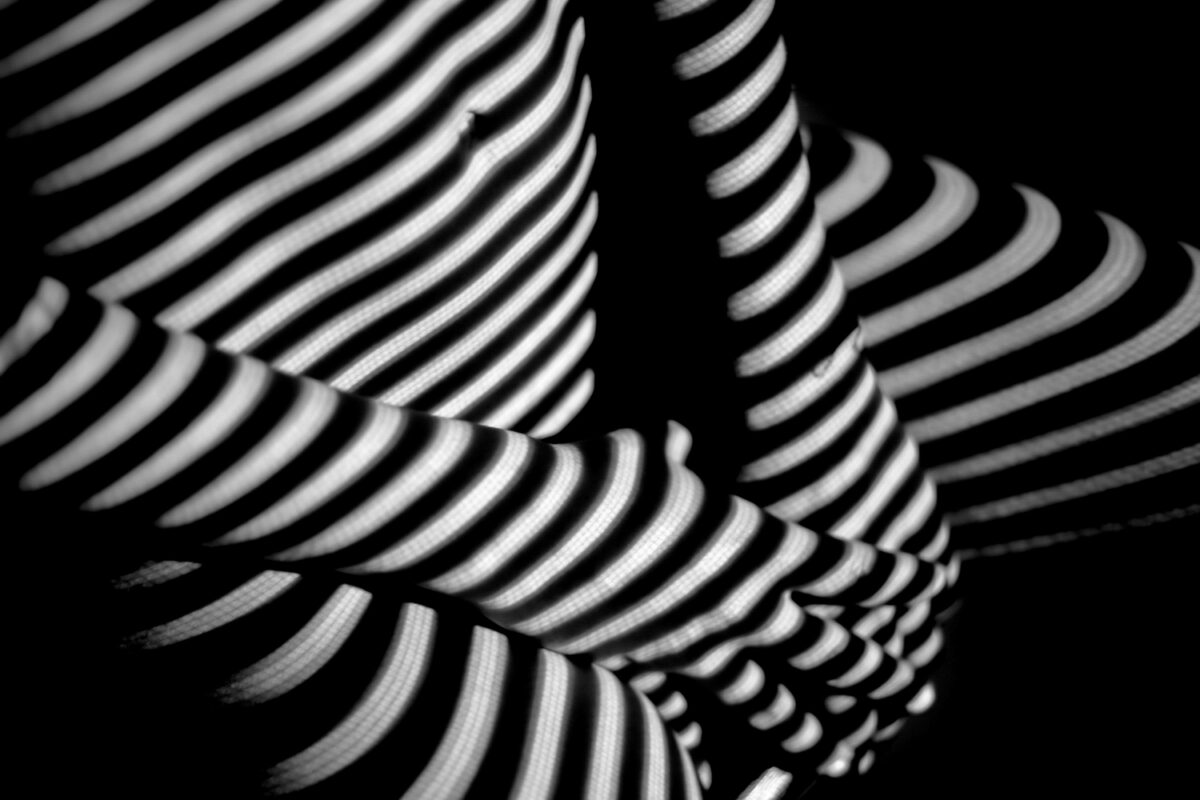 Corps humain éclairé par des ombres de rayures lumineuses, créant un motif abstrait en noir et blanc